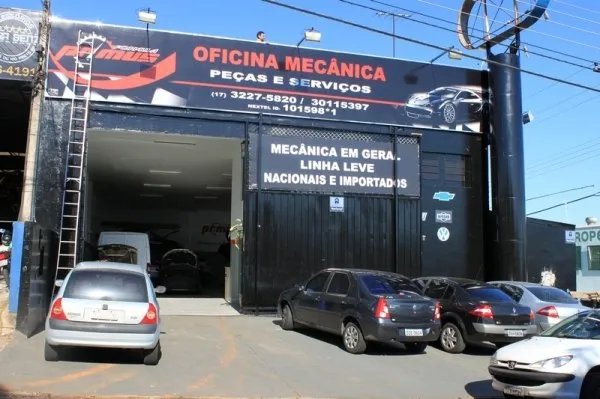 Fachada azul-escura da Fórmula Primus, com o letreiro Oficina Mecânica em vermelho e carros estacionados na calçada
