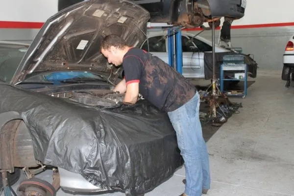 Mecânico debruçado sobre o compartimento do motor de um carro com o capô aberto