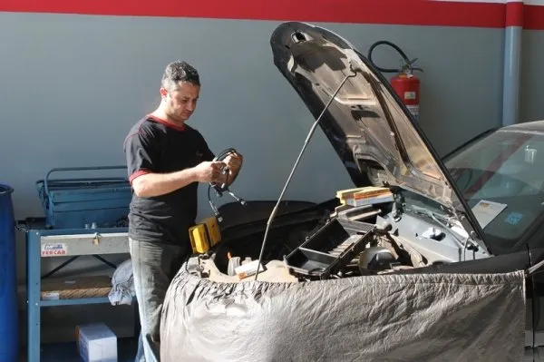 Mecânico conferindo o motor de um carro com o capô aberto e a frente protegida por capa