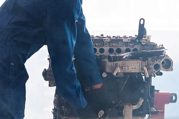 Mecânico de uniforme azul segurando um bloco de motor desmontado